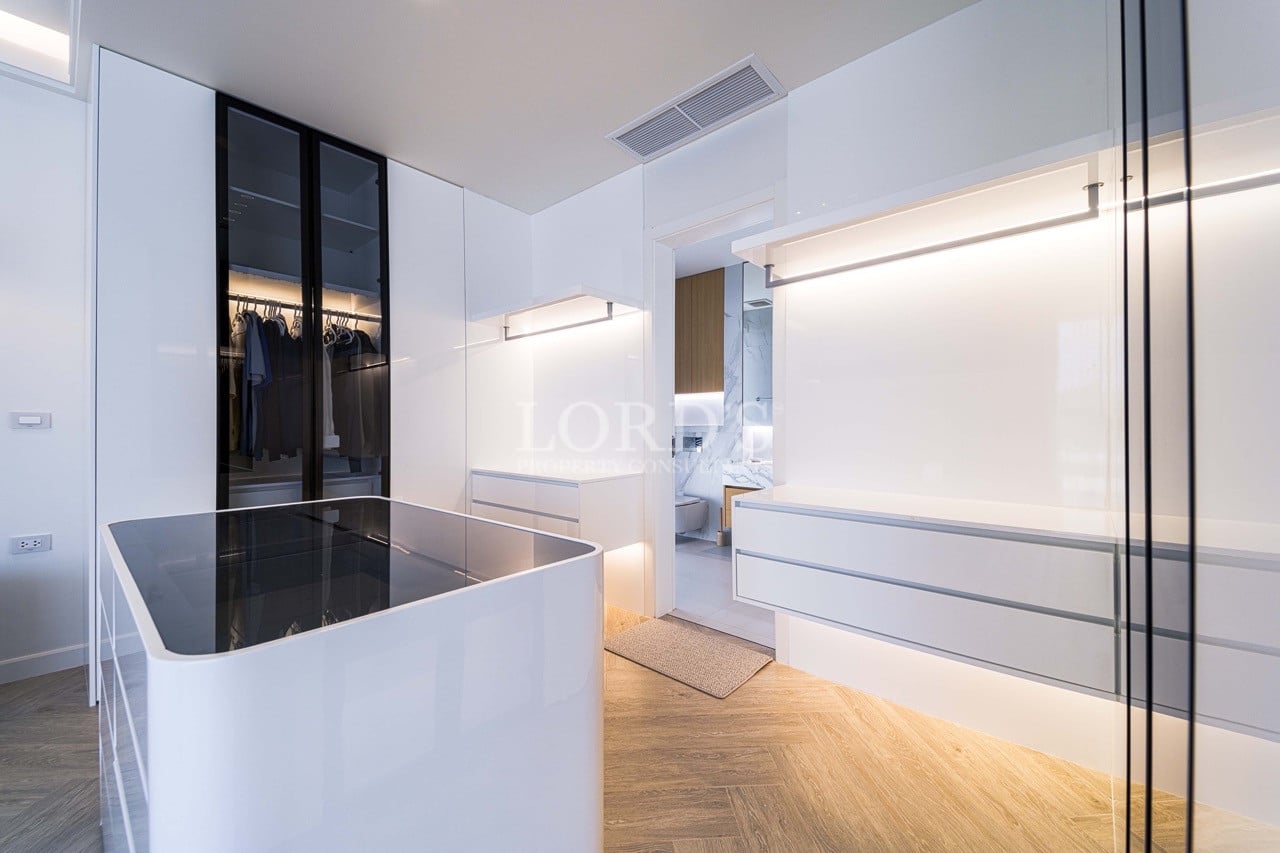 Luxury walk-in wardrobe with glossy white cabinets, glass-front closets, illuminated shelving, and central island.