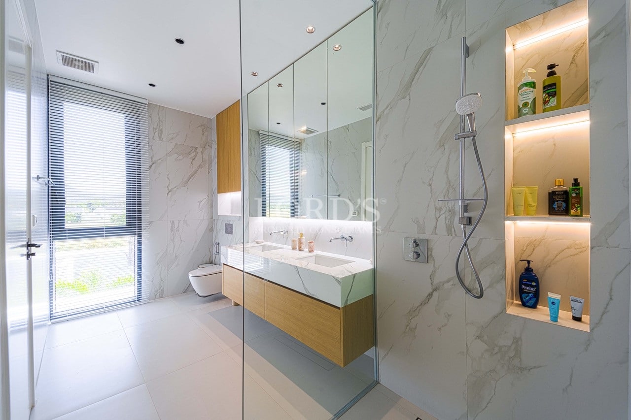 Modern luxury bathroom with marble walls, glass shower enclosure, floating vanity, and built-in illuminated shelves.