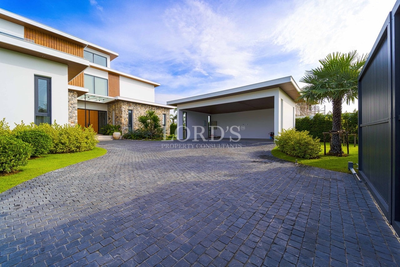 Modern villa driveway with stone-paved courtyard, covered carport, landscaped lawn, and contemporary exterior design.