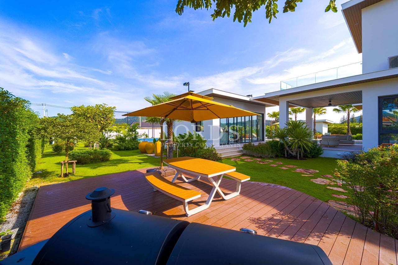 Outdoor garden deck with picnic table, sun umbrella, landscaped lawn, and modern villa seating area.