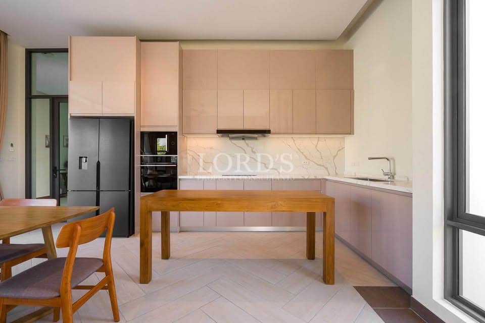 Modern kitchen with beige cabinetry, wooden dining table, and built-in appliances.