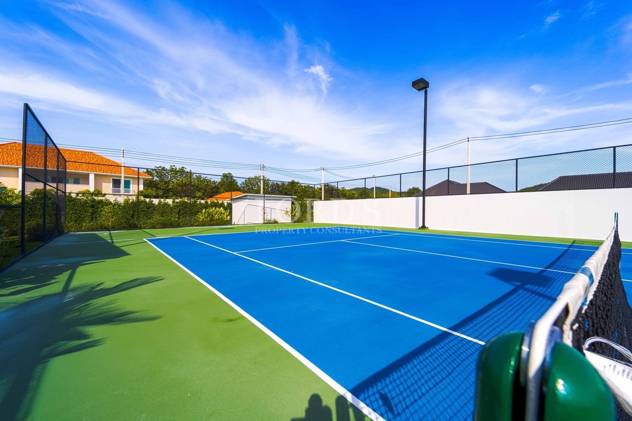Private full-size tennis court with blue playing surface, green outer court, perimeter fencing, and residential surroundings.