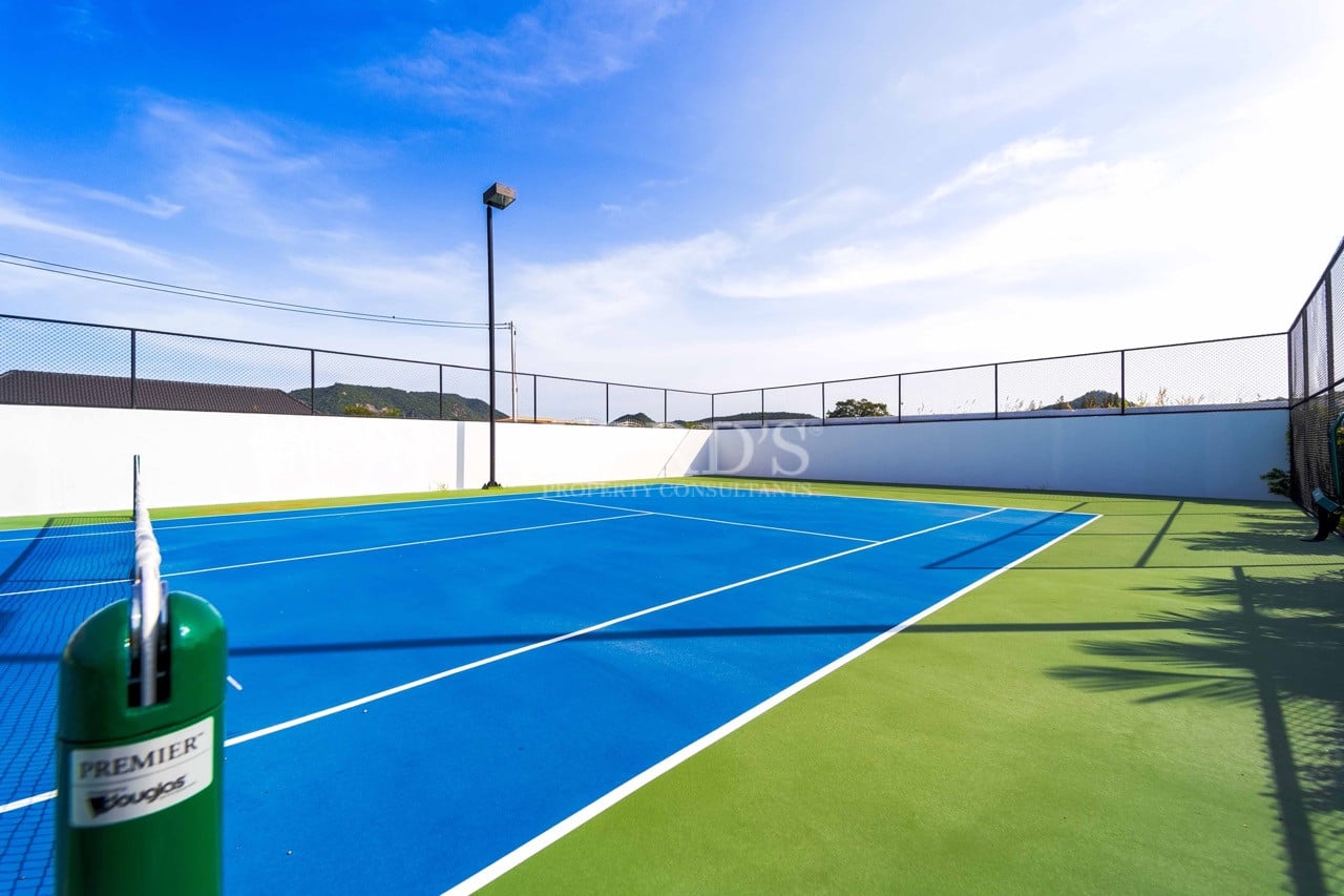 Private outdoor tennis court with blue and green surface, perimeter fencing, and scenic mountain views.