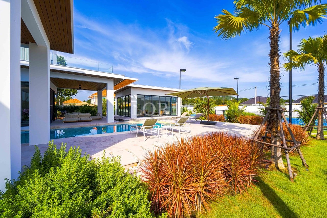 Luxury villa poolside terrace with sun loungers, palm trees, landscaped garden, and modern open-plan architecture.