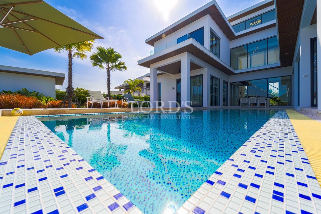 Modern luxury villa with private swimming pool, palm trees, and expansive glass walls under bright blue sky.