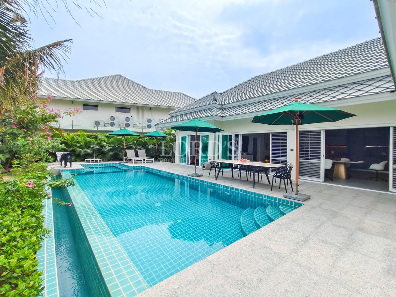 Private pool villa with spacious swimming pool, outdoor dining area, green umbrellas, and tropical garden.