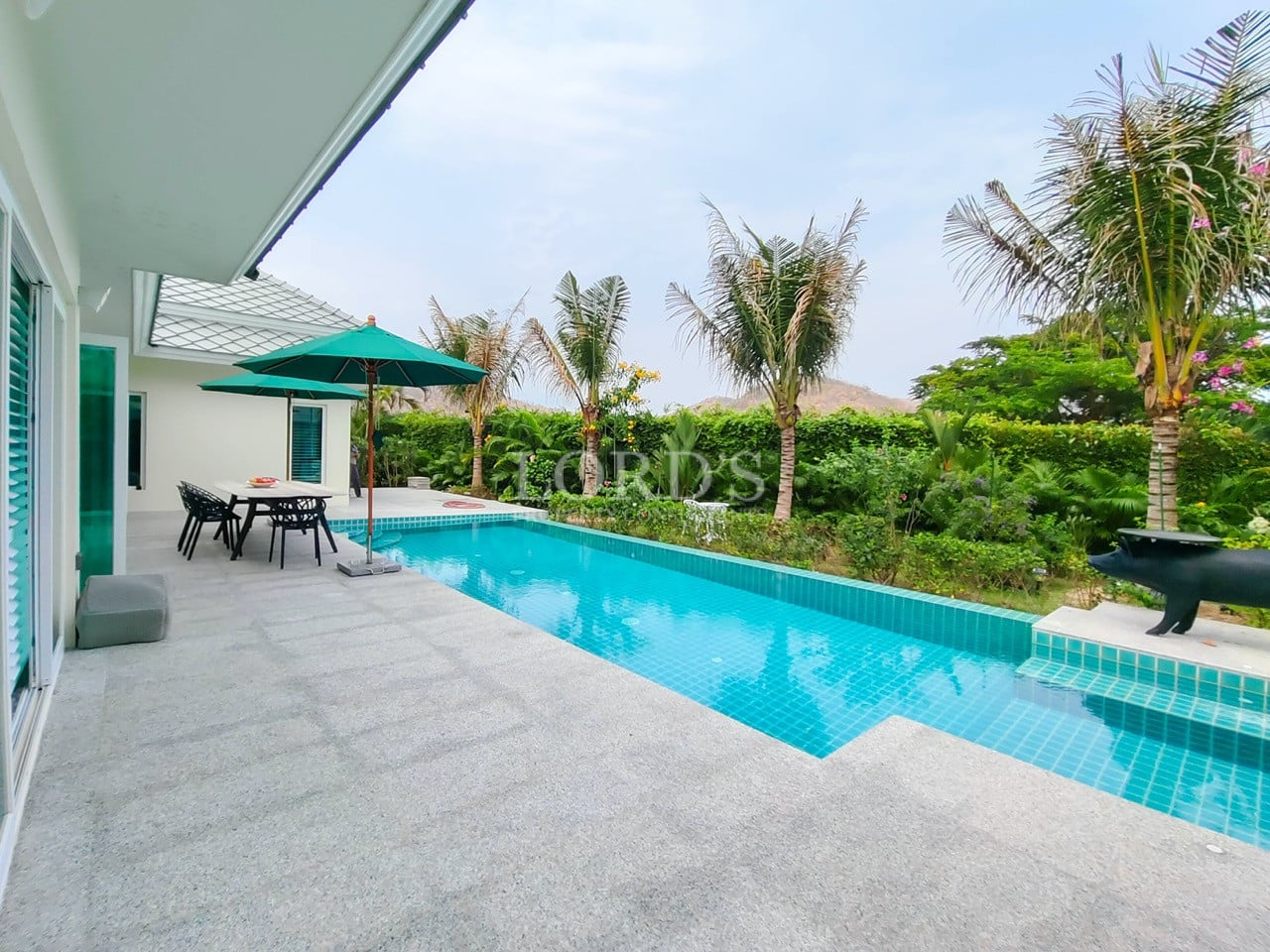 Long private swimming pool with poolside dining, shaded umbrella, and lush tropical garden.