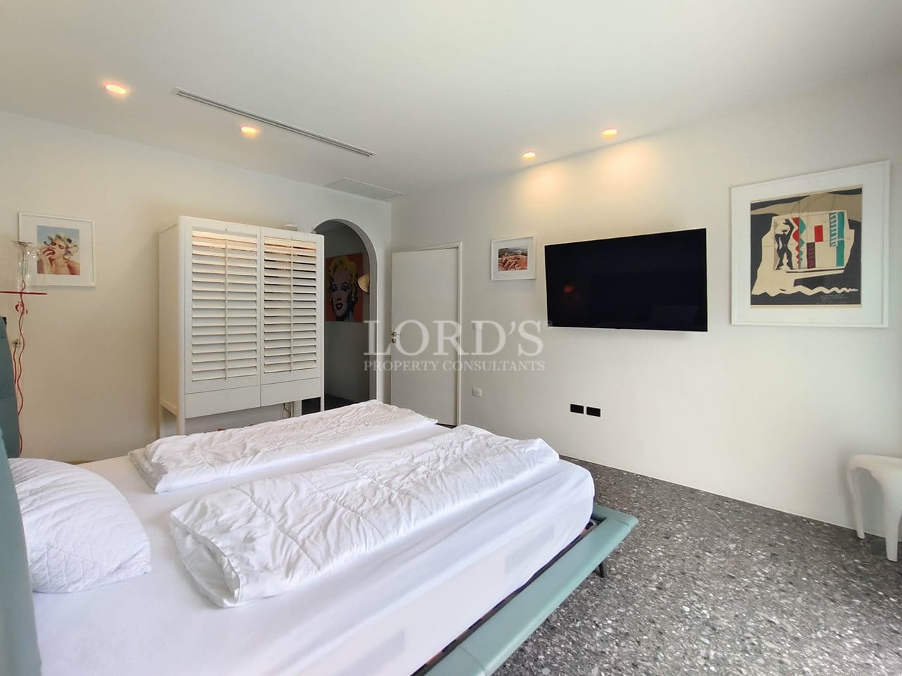 Modern bedroom with double bed, wall-mounted TV, minimalist furniture, and contemporary artwork.