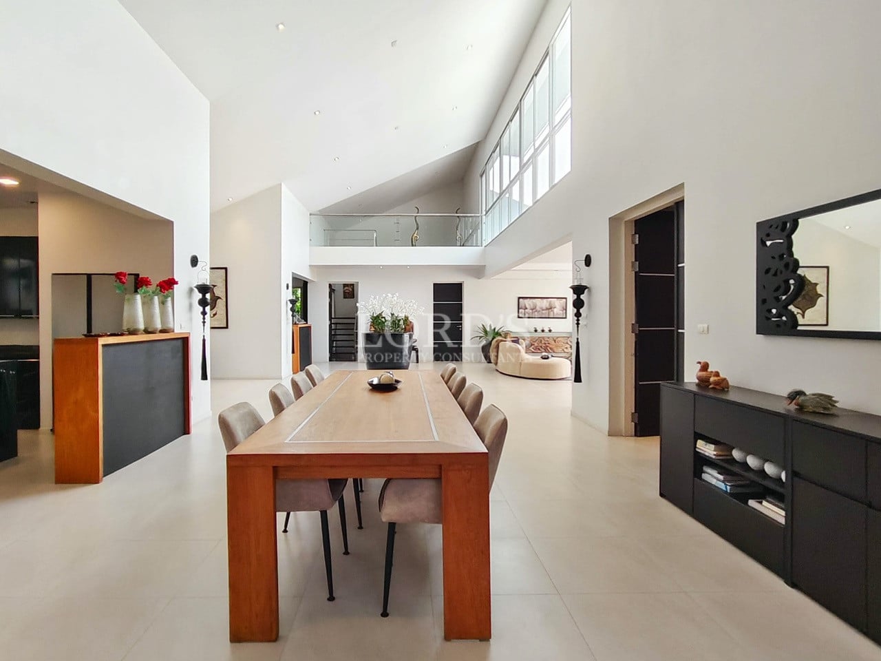 Spacious open-plan dining area with long wooden table and double-height ceiling.