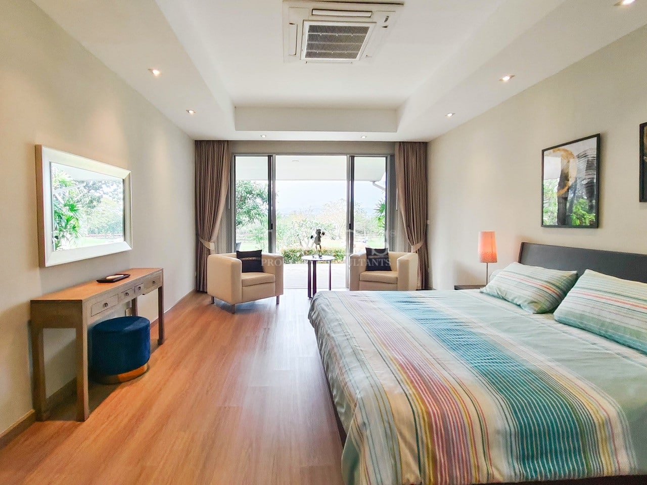 Spacious master bedroom in a modern luxury villa with seating area and garden view.
