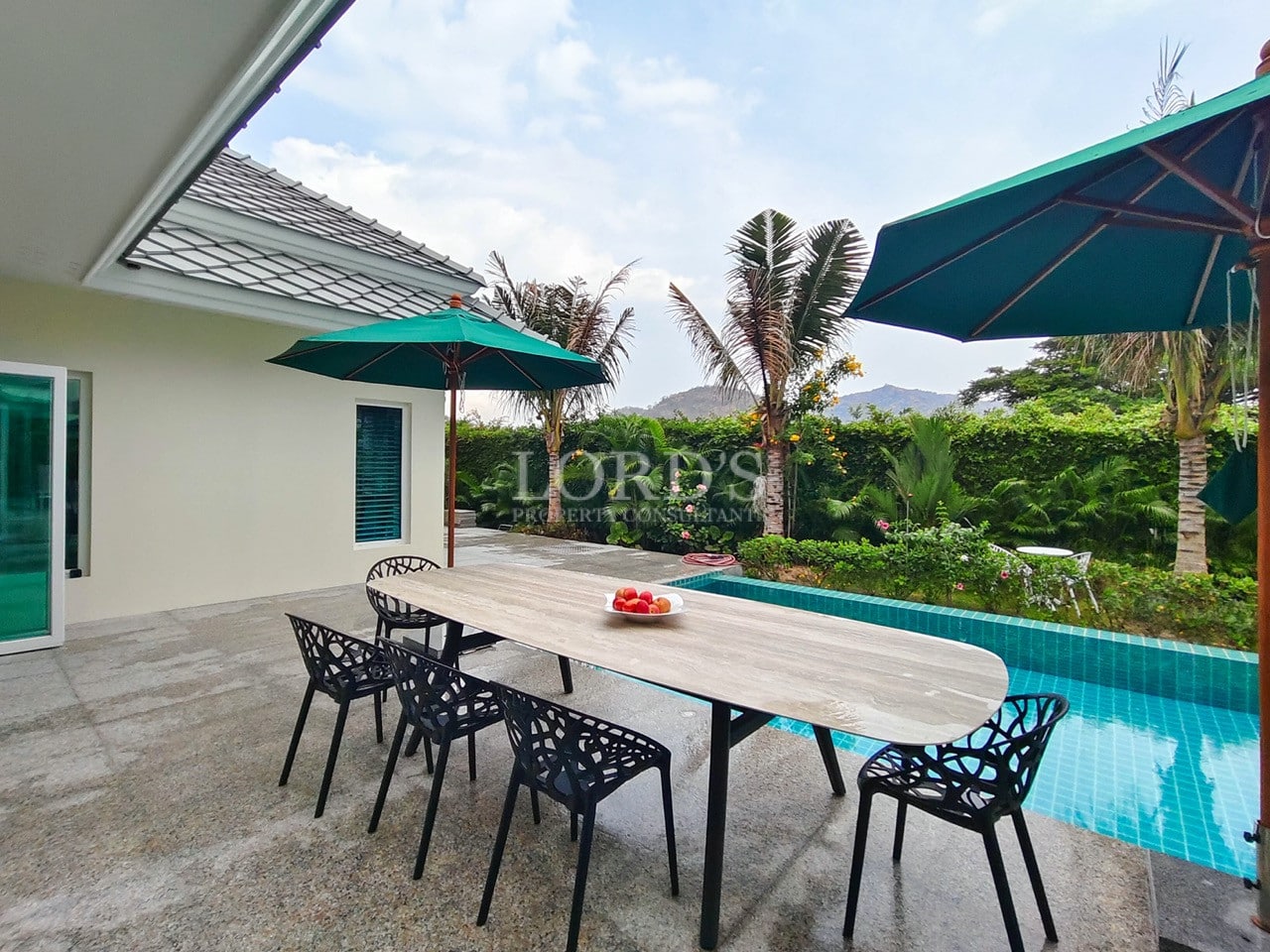 Outdoor dining area beside a private pool villa with umbrellas and tropical garden views.