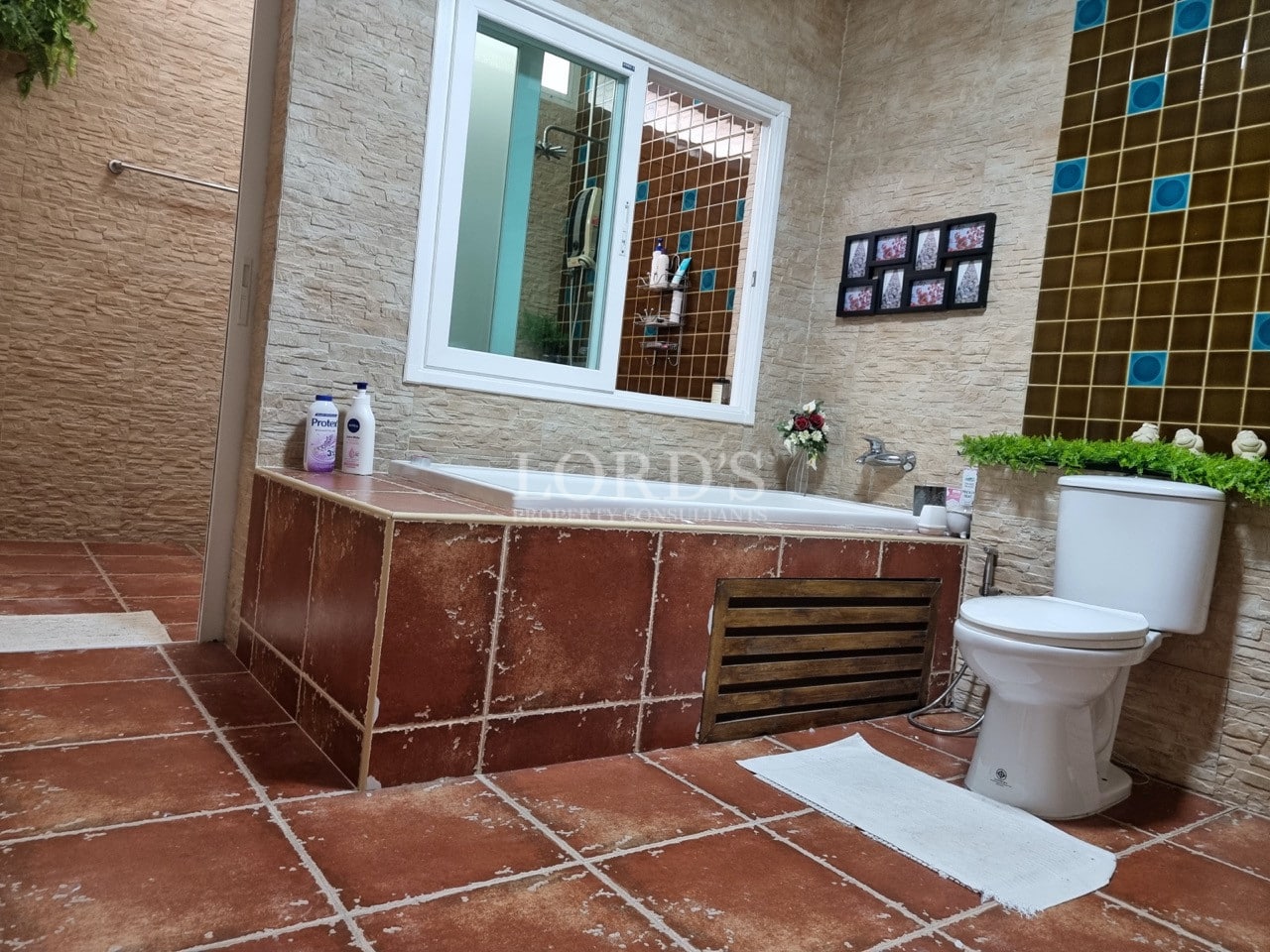 Bathroom with built-in tiled bathtub, stone-textured walls, modern toilet, and mosaic accent tiles.