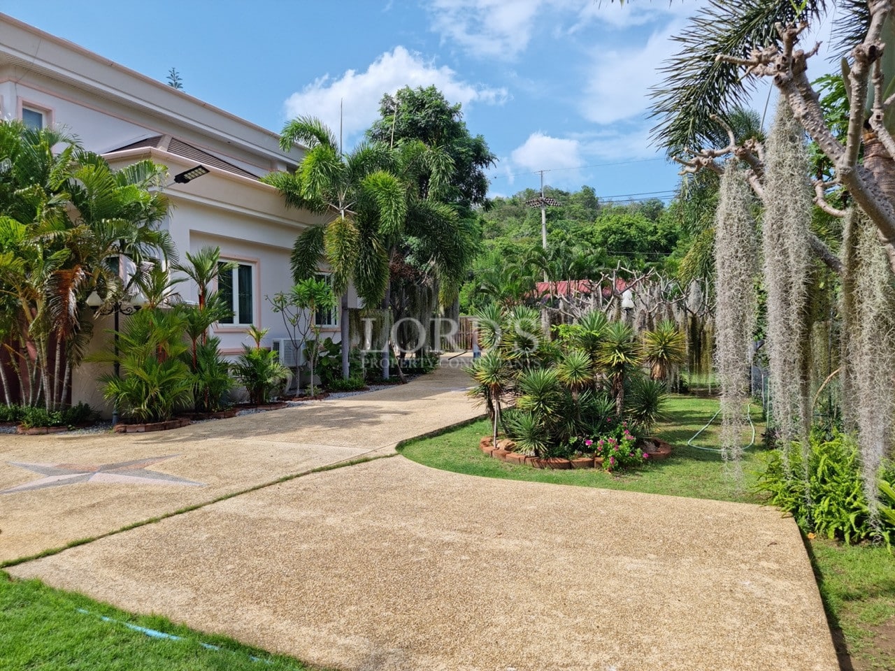 Luxury villa driveway with landscaped tropical garden, palm trees, and manicured greenery.