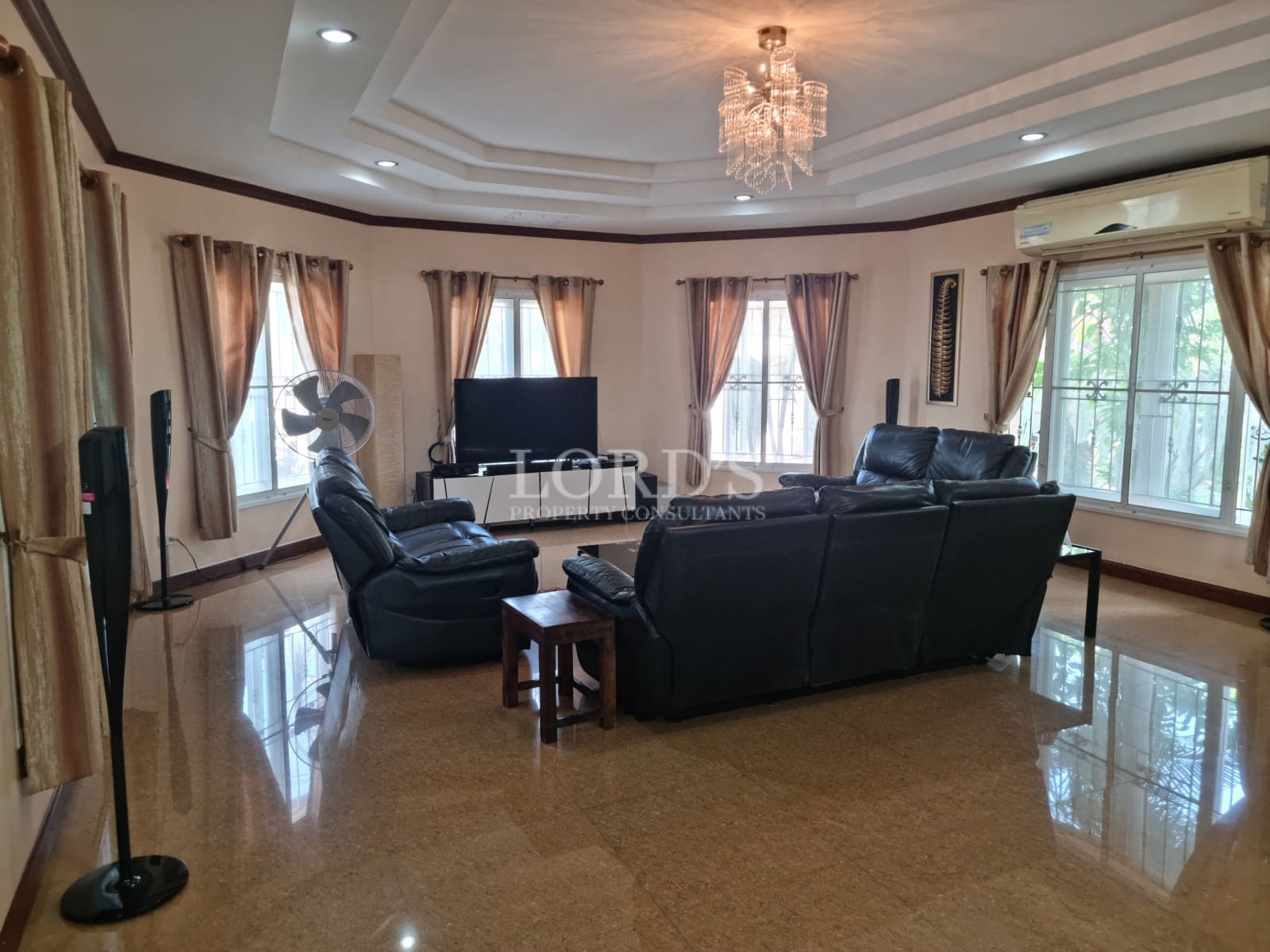 Luxury living room with leather sofas, chandelier lighting, large windows, and polished marble flooring.